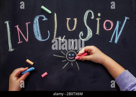 Inclusione di parola sulla lavagna nera della scuola scritta con gesso. Mani dei bambini, concetto di istruzione Foto Stock