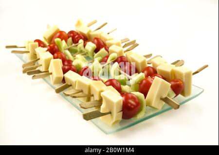 Formaggi, pomodori e stuzzichini cetrioli mini spiedini su piatto trasparente, sfondo bianco. Foto Stock