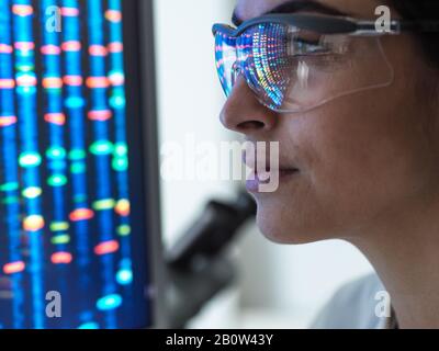 Ricerca genetica, scienziato femminile che osserva un profilo di DNA di un campione umano su uno schermo del laboratorio. Foto Stock
