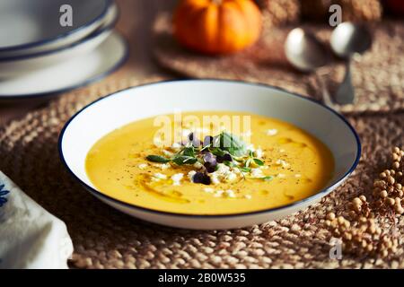 Angolo elevato primo piano della ciotola di zuppa di zucca con guarnitura su stuoia rustica. Foto Stock