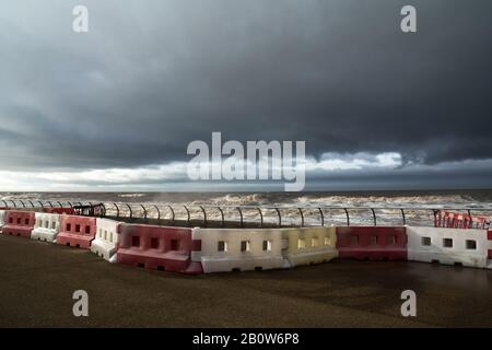 Le barriere di sicurezza in plastica rossa e bianca fiancheggiano il fronte mare come una tempesta. Foto Stock