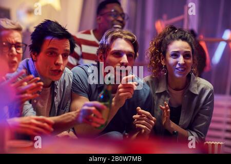 Gruppo di giovani tifosi seduti sul divano bere birra e guardare una partita di calcio insieme in TV a casa Foto Stock