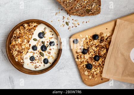 Ciotola di muesli e mirtilli su yogurt, pane multi-seme Foto Stock