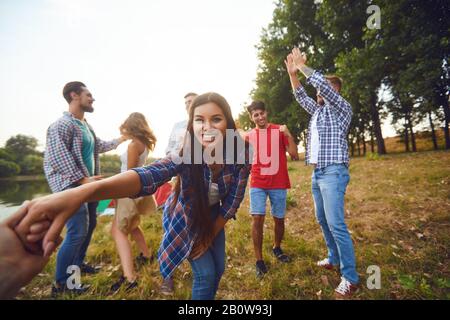 Gli amici hanno divertimento che corre lungo il lago su un picnic. Foto Stock