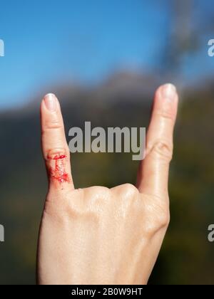 Foto di closeup di una mano di una donna con due dita sollevate indicando la roccia e rotolare su sfondo sfocato Foto Stock