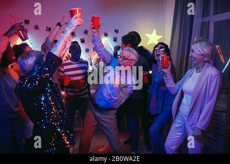 Uomo anziano beve birra e divertirsi con i giovani durante la festa a casa Foto Stock