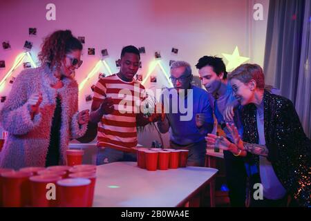 Uomo anziano che gioca nel gioco della birra pong insieme ai giovani durante la festa di casa Foto Stock