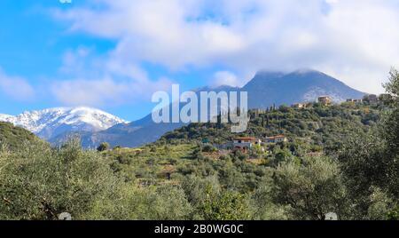 Case sul lato di una collina con la neve e nebbia coperta Taygetos catena montuosa in lontananza nel sud della Grecia Foto Stock