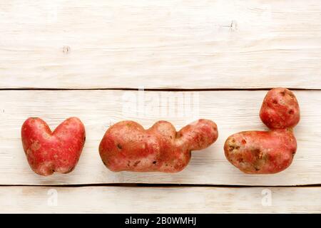 Verdure divertenti e brutte, patate a forma di cuore e forma di lettera su uno sfondo di legno bianco, primo piano. Vista dall'alto, spazio di copia. Foto Stock