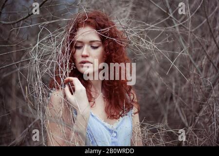 Donna con lunghi capelli rossi tra i rami, ritratto Foto Stock