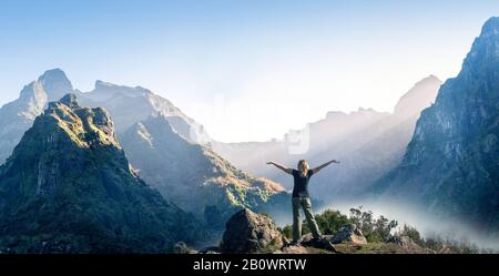 Donna Felice sorge con le mani alzate sullo sfondo del tramonto in montagna della gamma Foto Stock