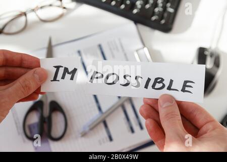 Mani d'uomo d'affari che tagliano la parola impossibile, lettere im in modo da diventa possibile. Concetto di successo e motivazione. Foto sul luogo di lavoro. Foto Stock