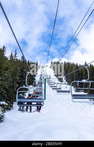 Identificabili gli sciatori e gli snowboarder sulla seggiovia andando su una pista da sci in montagna innevata gamma delle Canadian Rockies. Foto Stock