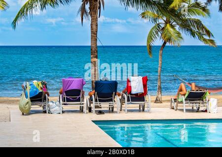 Le persone che si rilassano sulle sedie a sdraio tra una piscina e una spiaggia tropicale in una bella giornata. Foto Stock