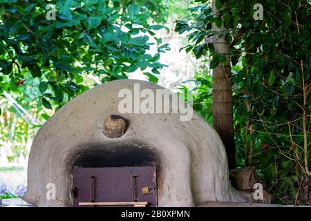 Una vecchia casa fatta terra pizza forno a legna fuori in un giardino coltivato, ora bloccato e inutilizzato, circondato da alberi Foto Stock