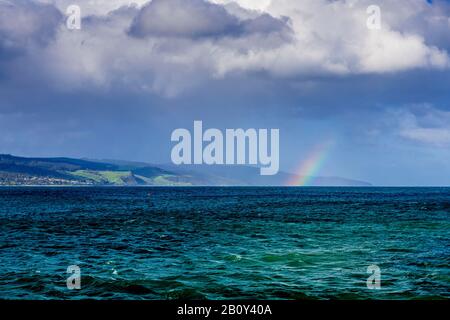 Apollo Bay con la pioggia che si avvicina causando la formazione di un piccolo arcobaleno sull'acqua. Victoria, Australia Foto Stock