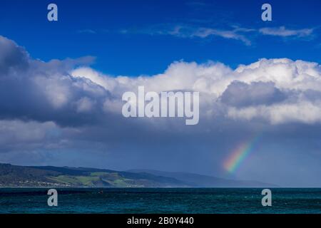 Apollo Bay con la pioggia che si avvicina causando la formazione di un piccolo arcobaleno sull'acqua. Victoria, Australia Foto Stock