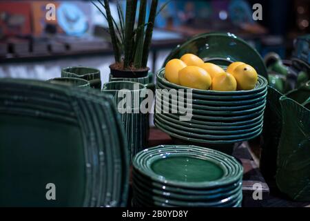 Piastre in ceramica verde con limoni su un ripiano in un negozio. Piastre di design con un motivo. Impostazione del tavolo, stoviglie e concetto di cibo. Vari tipi di Foto Stock