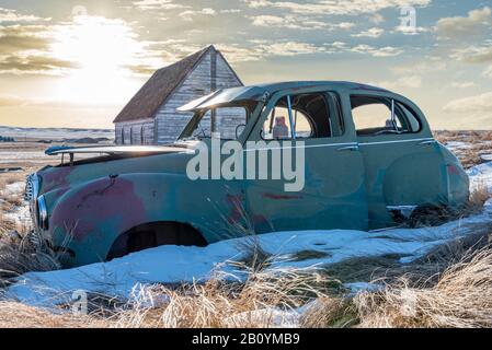 Auto abbandonata e chiesa su una collina innevata che si affaccia su due ascensori a grano gemello in Neidpath, SK Foto Stock