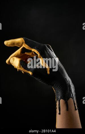 Mano femminile raffinata cosparsa di vernice acrilica nera e oro su fondo nero Foto Stock