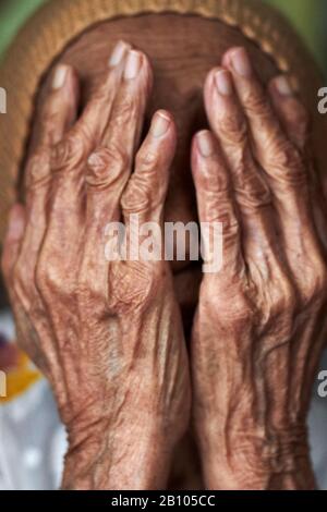 Ritratto di una donna malese anziana che copre il suo viso con le sue mani rugose Foto Stock