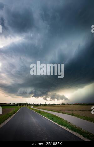 Nube muraria a bassa sospensione, base in buona salute e nucleo di precipitazioni pesanti di una classica supercella su una strada di campagna vicino Heilsbronn, Baviera, Germania Foto Stock