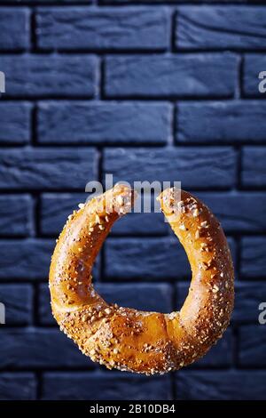 Un kifli o kipfel austriaco a forma di mezzaluna cosparso di arachidi e zucchero a velo davanti a una parete di mattoni neri, spazio per le copie, orientamento verticale Foto Stock