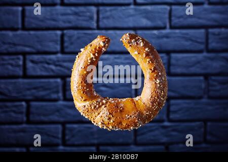 Un singolo kifli o kipfel austriaco a forma di mezzaluna cosparso di arachidi e zucchero a velo di fronte alla parete di mattoni neri, copia spazio, orientat orizzontale Foto Stock