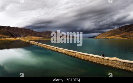 I monaci buddisti si pedalano su una motocicletta sopra un bacino di acqua sull'altopiano tibetano, provincia del Sichuan, Cina Foto Stock