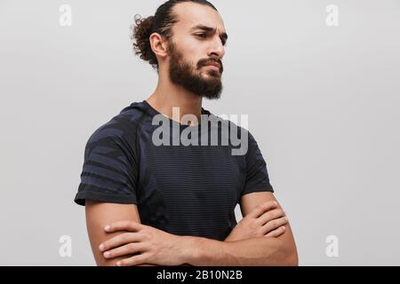 Immagine di giovane sportivo unshaven che indossa tuta in piedi con le braccia incrociate isolato su sfondo bianco Foto Stock