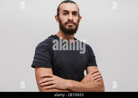 Immagine di giovane sportivo unshaven che indossa tuta in piedi con le braccia incrociate isolato su sfondo bianco Foto Stock