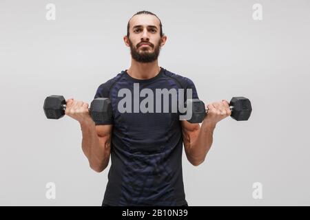 Immagine di giovane bruna sportivo che indossa tuta sollevamento manubri isolato su sfondo bianco Foto Stock