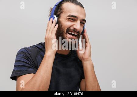 Immagine di giovane sportivo felice indossando tuta sorridente mentre ascolta la musica con cuffie isolate su sfondo bianco Foto Stock