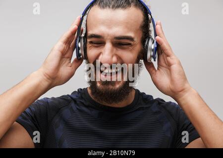 Immagine di giovane sportivo felice indossando tuta sorridente mentre ascolta la musica con cuffie isolate su sfondo bianco Foto Stock