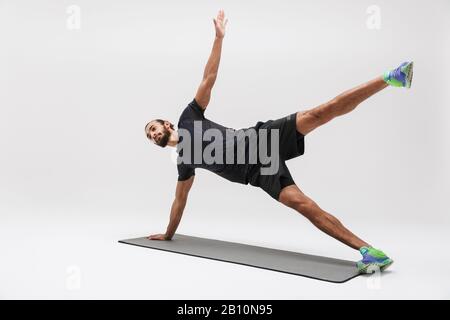 Immagine di attraente sportivo brunette in tuta facendo esercizio su tappeto yoga isolato su sfondo bianco Foto Stock