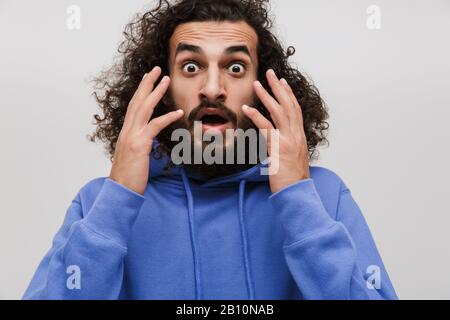 Immagine di un uomo impaurito in una felpa casual che esprime meraviglia alla macchina fotografica isolata su sfondo bianco Foto Stock