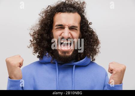 Immagine di un uomo felice senza barba in una felpa casual che urla con pugni che si stringe isolati su sfondo bianco Foto Stock