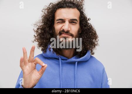 Immagine di uomo felice unshaven in felpa casual gesturing segno okay con le dita isolato su sfondo bianco Foto Stock