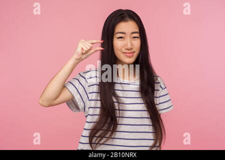 Ritratto di ragazza positiva con capelli castani che mostrano un po ', piccolo gesto e guardare la fotocamera con espressione delusa, mostrando mini Foto Stock