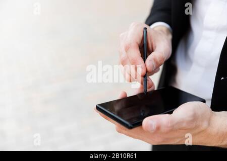 Primo piano di un uomo d'affari utilizzando cellulare e stilo all'aperto Foto Stock