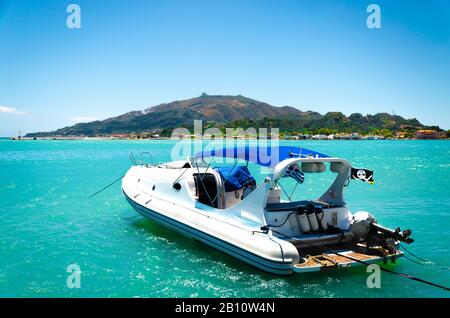 Barca in acque azzurre del mare con isola verde sullo sfondo. Tour in barca sul mare. Viaggi estivi. Foto Stock