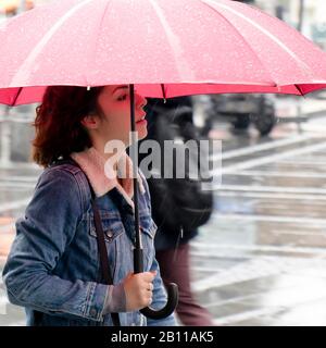 Belgrado, Serbia - 24 settembre 2019: Una giovane donna in giacca denim che cammina sotto ombrello rosso in una giornata piovosa Foto Stock