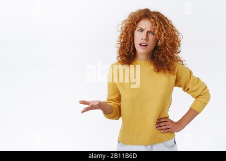 Frustrato, messo in discussione maledhead donna maledetta in maglione giallo avendo argomento, incomprensione, accigliarsi, sollevare una mano in dismaggio staring infastidito Foto Stock