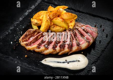 carne e patate fritte affettate in modo rustico su uno sfondo nero testurizzato Foto Stock