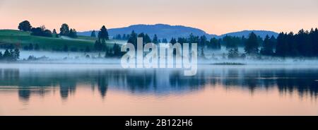 Nebbia mattutina all'alba su Bannwaldsee vicino a Füssen, Allgäu, Baviera, Germania Foto Stock