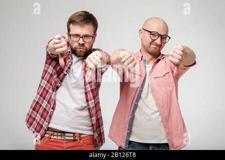 Due uomini, che mostrano un cattivo segno e dissimile, fanno un gesto con il pollice giù, con una grimace di disapprovazione sul loro volto. Foto Stock