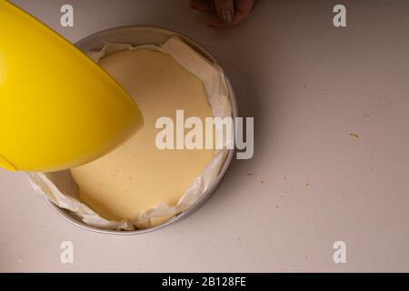 Donna che versa l'impasto per una torta in uno stampo di alluminio imbottito con carta pergamena. Foto Stock