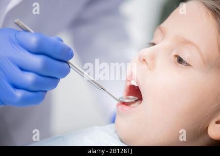 Mano gloved del dentista che esamina i denti del piccolo paziente cute con lo specchio dentale Foto Stock