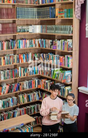 Ragazzo intelligente adolescente che punta alla copertina del libro tenuto dal suo compagno di classe Foto Stock