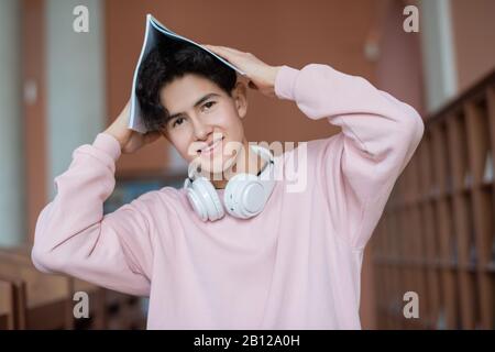 Felice adolescente che tiene copybook sopra la testa mentre sta davanti alla macchina fotografica Foto Stock